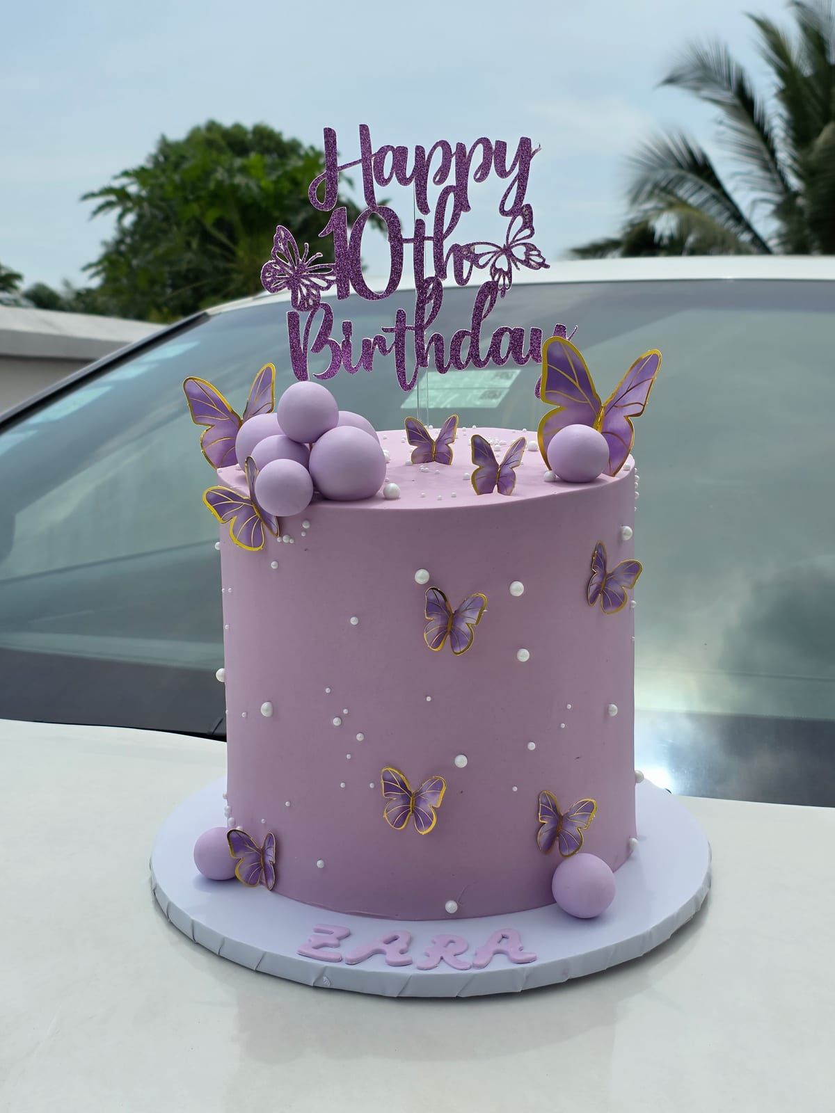 Tall lilac cake with purple and white spheres, sugar butterflies climbing one side and a purple script topper