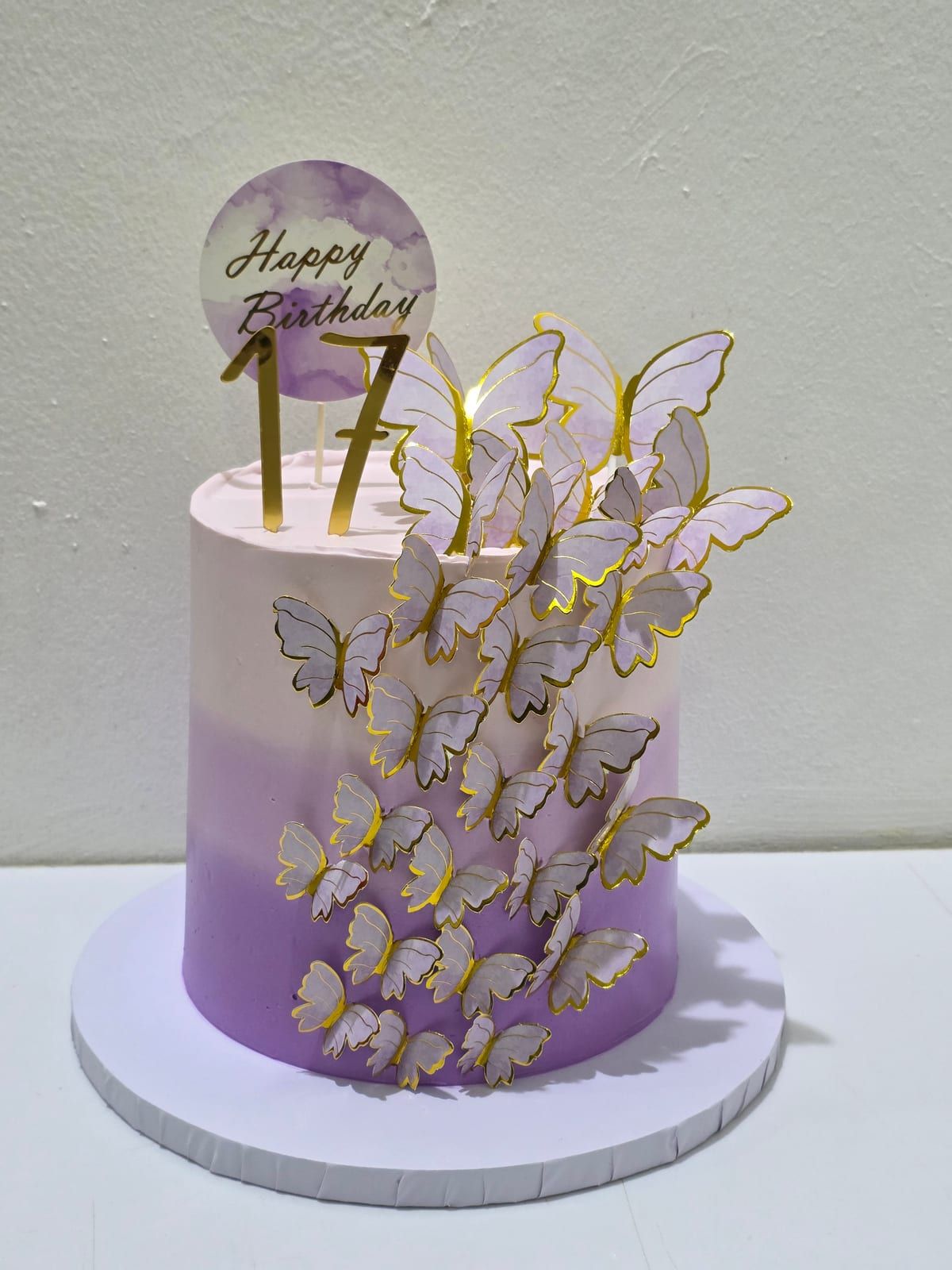 Tall cake shading from pale pink at the top to purple at the base, with a cascade of gold-edged white butterflies down one side, a gold "17" and a round "Happy Birthday" topper