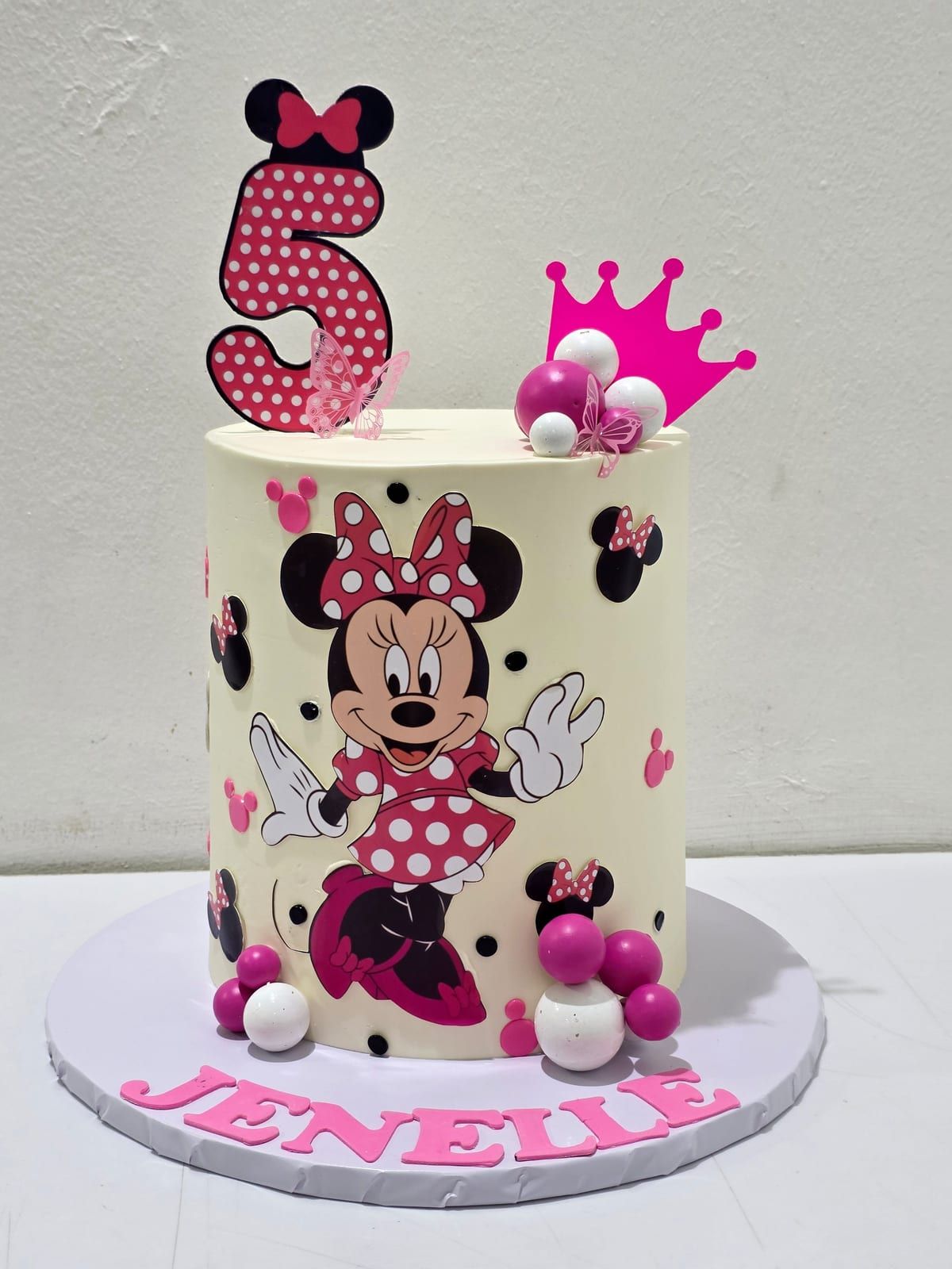Tall ivory cake with pink and black polka dots, a large modelled cartoon-mouse figure, a pink numeral and a crown topper